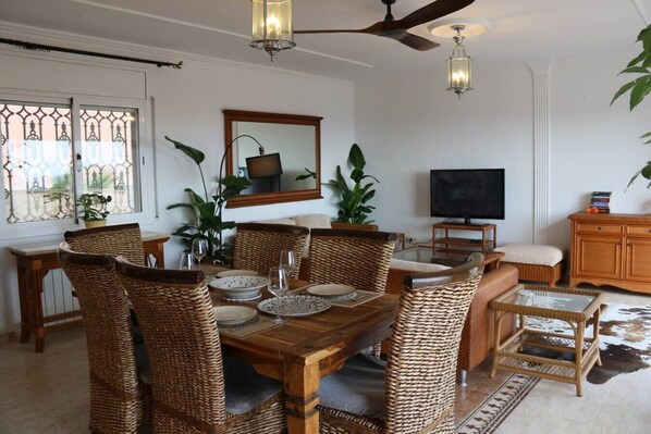Un comedor con muebles de mimbre, un televisor y un ventilador de techo.
