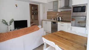 Eine kleine Küche mit weißen Schränken, einem Holztisch, einer eingebauten Mikrowelle und einem Fernseher.