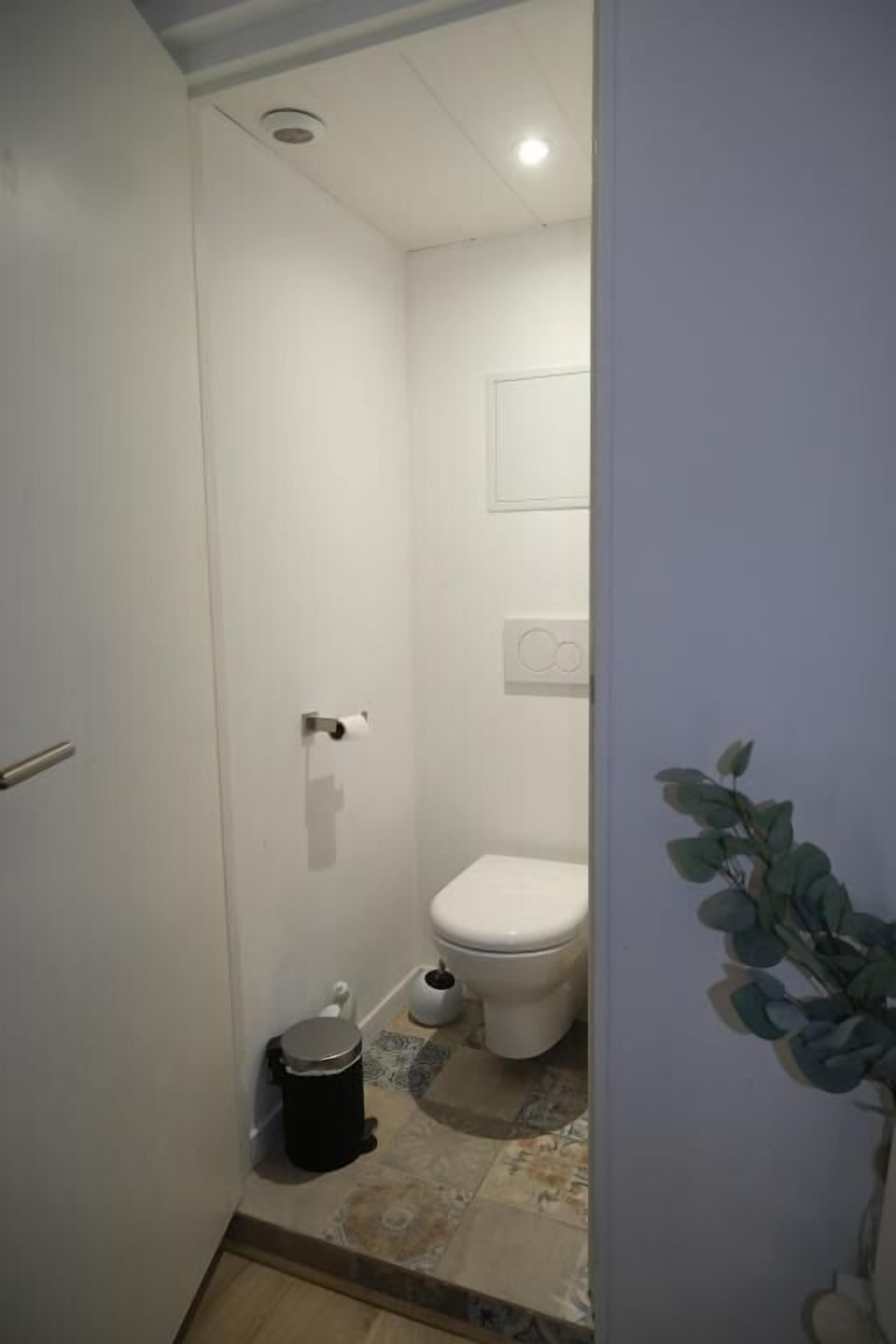 A small, narrow bathroom with a toilet, a trash bin, and a tiled floor.