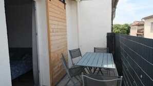 Ein Balkon mit Tisch und Stühlen, eine Holztür und ein schwarzer Zaun.