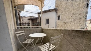 Un balcone con tavolo e due sedie, un muro in pietra e vista sugli edifici circostanti.