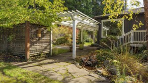 Ein Steinweg führt zu einer hölzernen Pergola und einem Holzbau mit einem Fenster.
