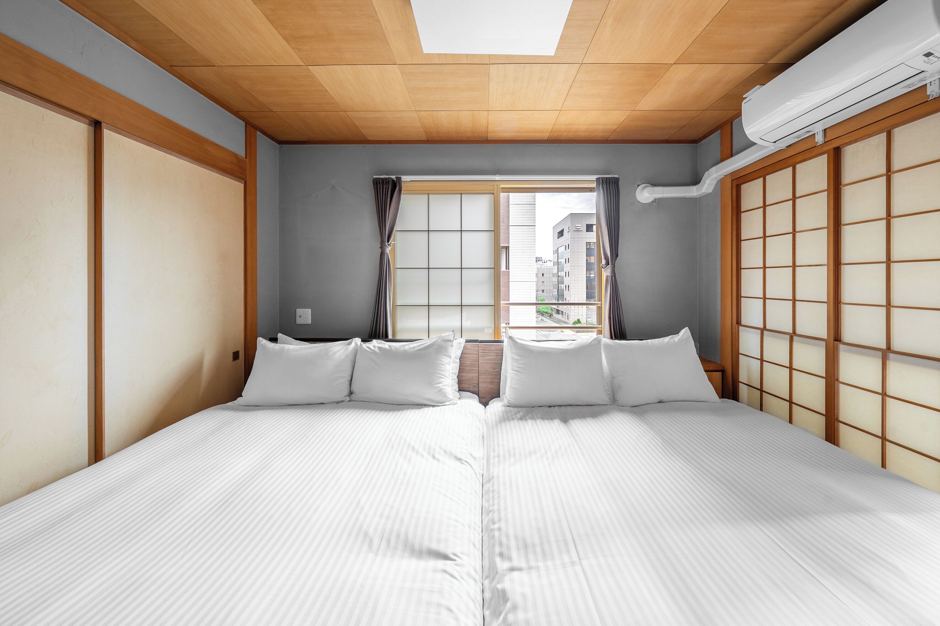 A hotel room with a traditional Japanese-style sliding door, a large window with curtains, and a ceiling fan.