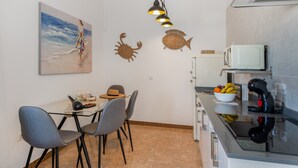 A modern kitchen with a microwave, coffee maker, and fruit bowl. There is a dining area with chairs and a table, and a painting of a beach scene. - Holiday Home '2' with Wi-Fi and Air Conditioning (El Golfo)