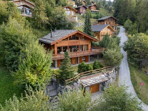 Een houten chalet met balkon, omringd door weelderige begroeiing en een bergpad.