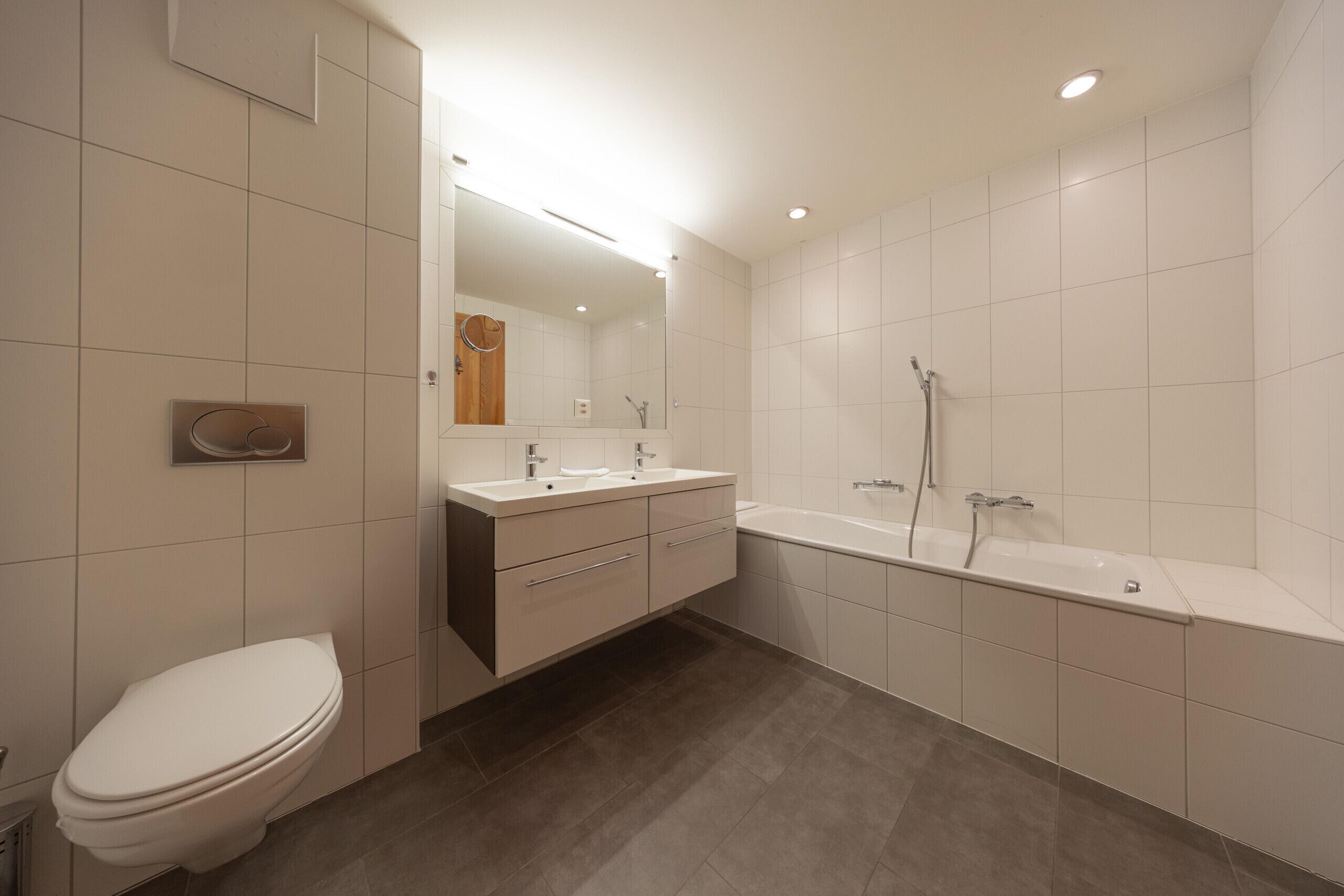 A modern bathroom with a toilet, a sink, a mirror, and a bathtub.