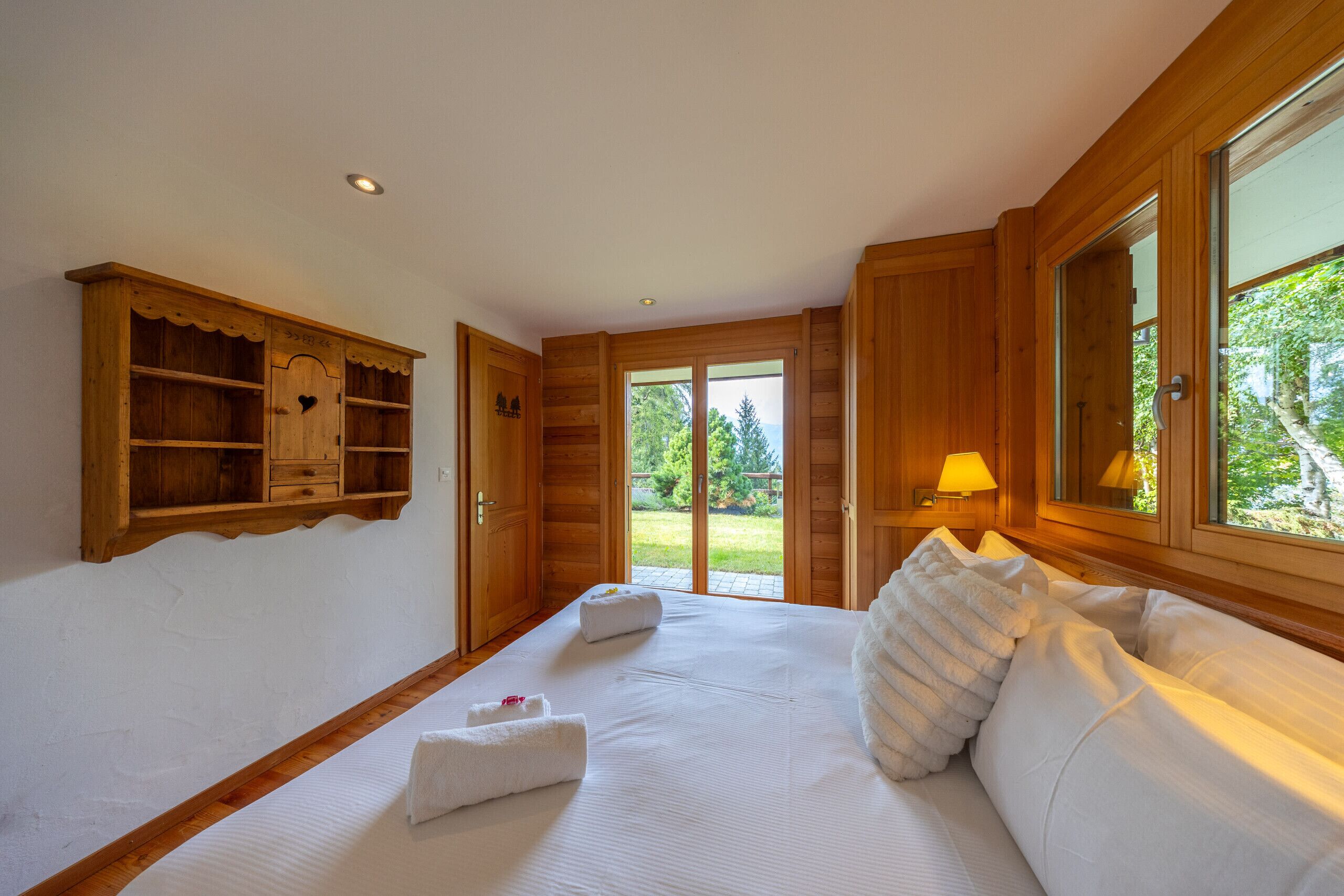 Dormitorio con estructura de madera, cama grande, aparador de madera y vista a la vegetación a través de la puerta.