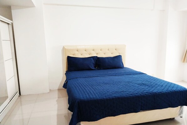 Une chambre à coucher avec un lit, une tête de lit blanche et une couvre-lit bleue.