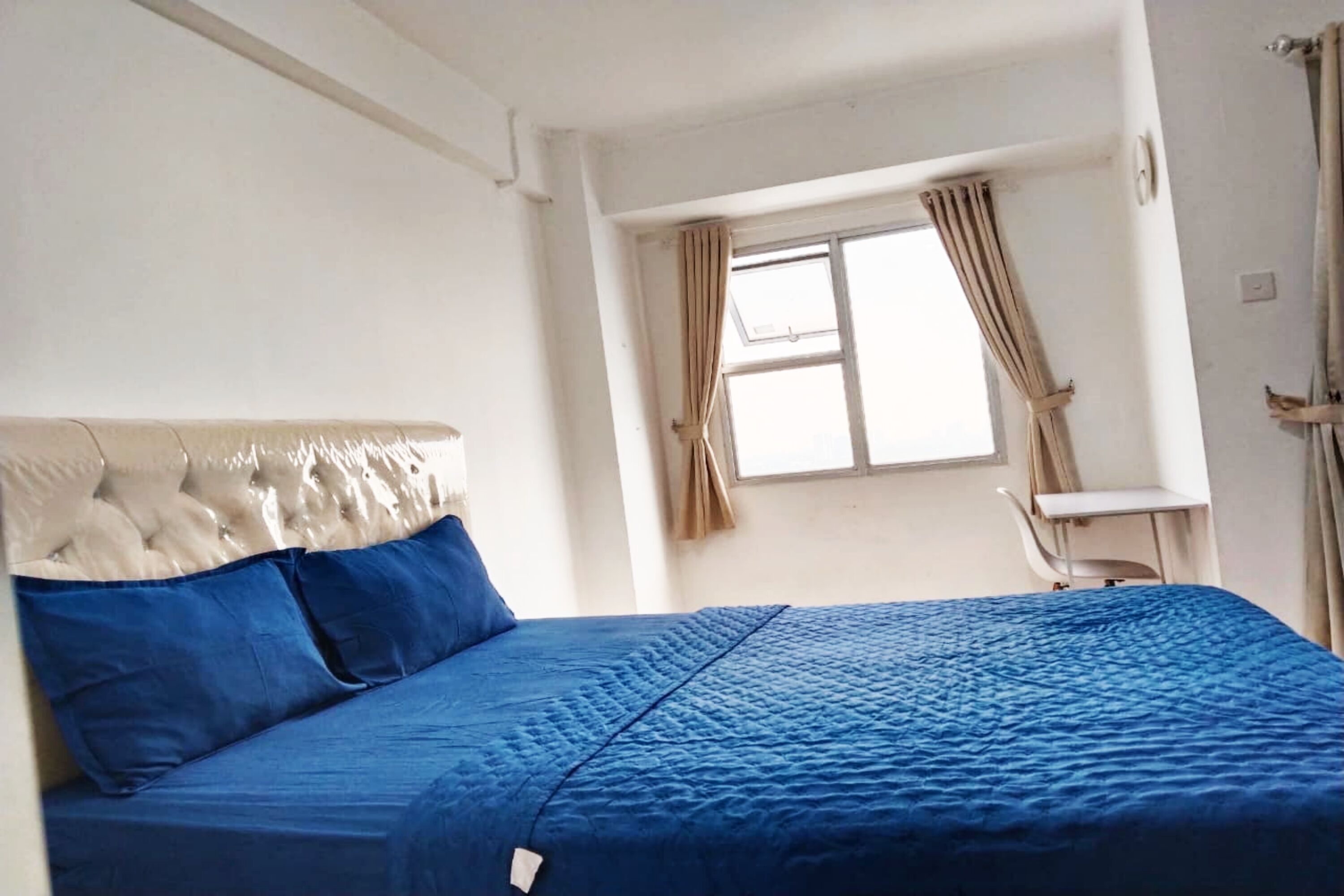 A room with a bed, a window with curtains, a chair, and a small table.