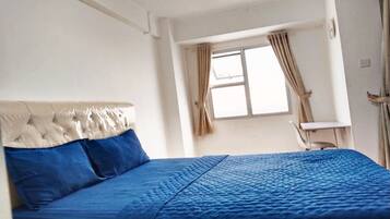 A room with a bed, a window with curtains, a chair, and a small table.