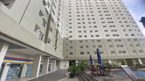 Ένα πολυώροφο ξενοδοχείο με πολλούς ορόφους, έναν εξωτερικό χώρο με καθίσματα, καρέκλες και ομπρέλες, καθώς και μια πισίνα.