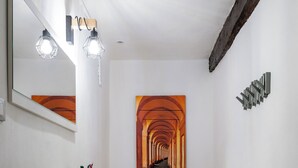 A hallway with a wooden floor, a white bench, a wall-mounted mirror, and a painting of a tunnel.