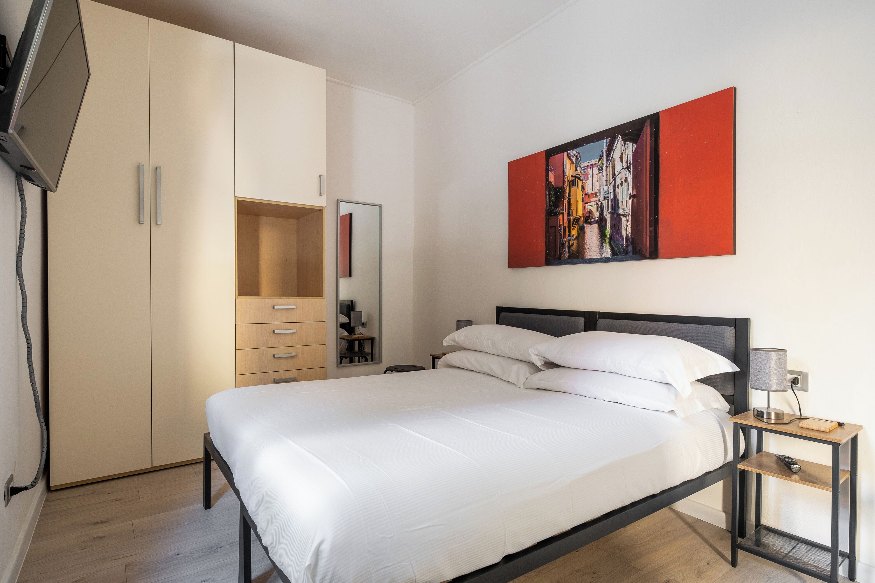 A bedroom with a bed, a bedside table with a lamp, a wardrobe, and a painting on the wall.