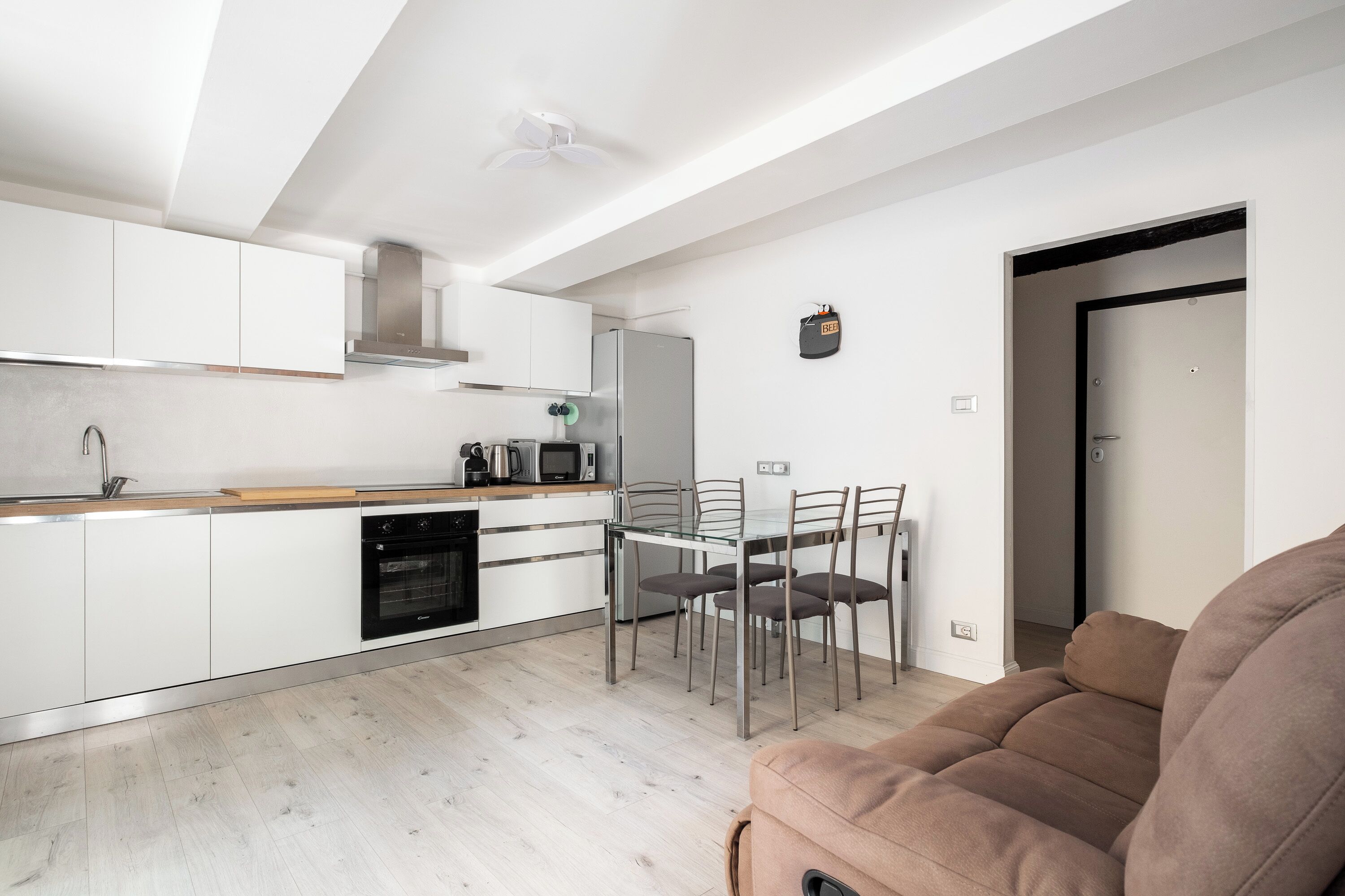 A modern kitchen with white cabinets, a stainless steel refrigerator, and a dining area with a glass table and metal chairs.