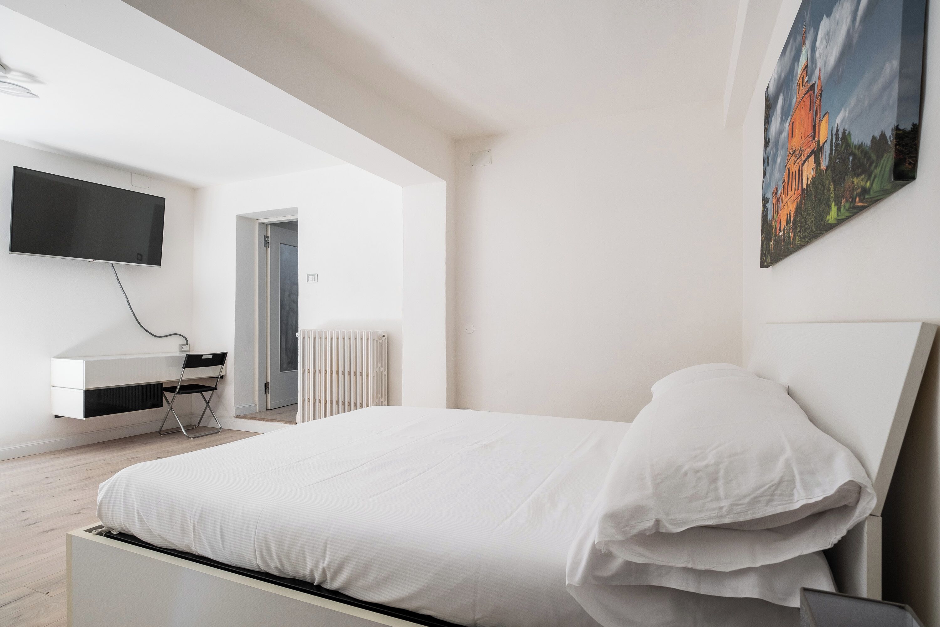 Un dormitorio moderno con una cama, un televisor montado en la pared y un cuadro.