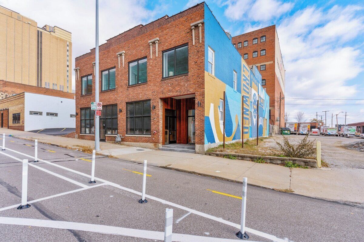 A multi-story building with a brick facade, large windows, and a colorful mural on the side.
