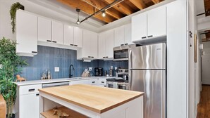A modern kitchen with white cabinets, a wooden island, stainless steel appliances, and a blue backsplash.