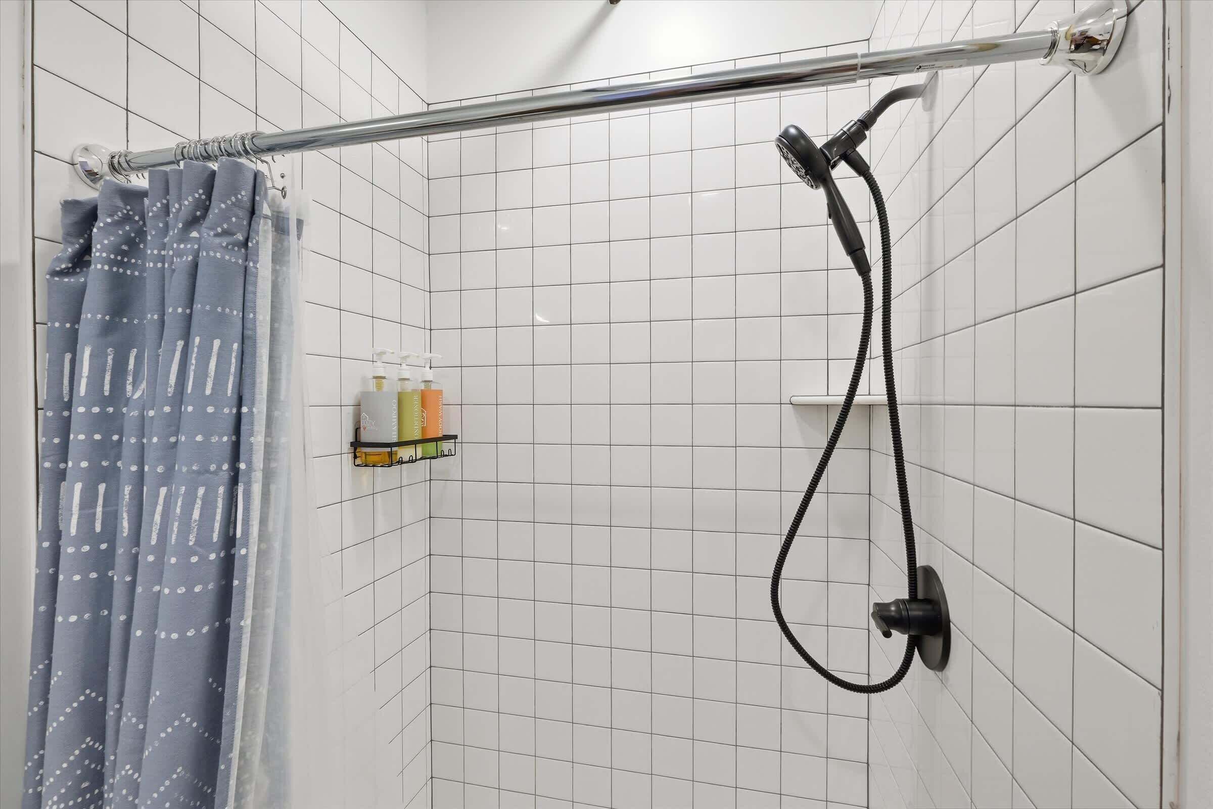 A shower area with a metal handrail, a showerhead, and a curtain.