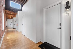 Un couloir avec des portes blanches, un extincteur et un paillasson noir.