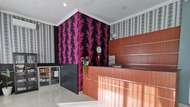 Un área de recepción con un mostrador de madera, una vitrina de vidrio y una pared con un diseño de hojas en tonos negros y rosados.