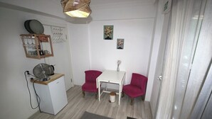 A small, compact room with a white table and two red chairs, a white refrigerator, a fan, and a small trash bin. - FETHİYE GARDEN HOUSE Apartment with private garden in the city center (Muğla)