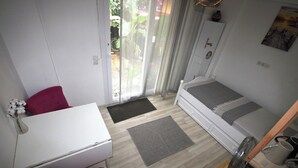 A compact room with a bed, a desk, and a chair. There is a window with a view of greenery outside. - FETHİYE GARDEN HOUSE Apartment with private garden in the city center (Muğla)