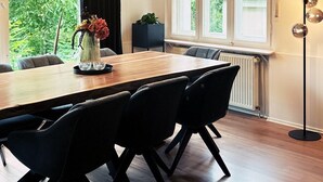 Een eetruimte met een houten tafel, zwarte stoelen en hangende lampen.