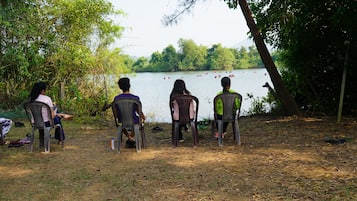 Three people seated on plastic chairs facing a lake with boats.