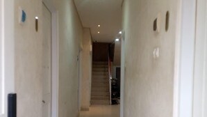 Um corredor estreito com piso de azulejos, paredes brancas e uma porta à esquerda.