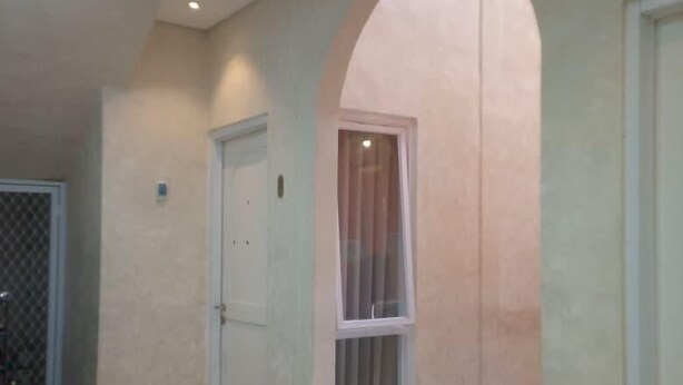 Um corredor amplo com teto alto, uma porta e uma janela com cortinas.