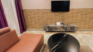 Ein Wohnzimmer mit einer Couch, einem Couchtisch, einem Flachbildfernseher an einer strukturierten Wand und einer kleinen Kommode mit Steckleiste.