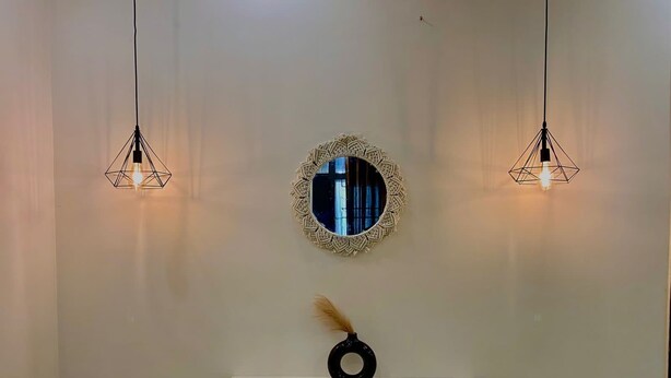 Eine Wand mit zwei Pendelleuchten, einem runden Spiegel und einem kleinen Tisch mit einem dekorativen Gegenstand.
