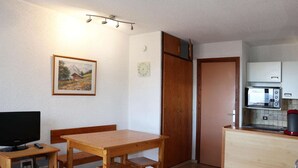 Un espacio habitable compacto con una mesa de comedor de madera, un televisor sobre un mueble, una kitchenette con microondas y una puerta que da a otra habitación.