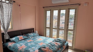 A bedroom with a bed, an air conditioner, a window with blinds, and a trash bin. - Soothing 3-bedroom apartment with AC in Bengaluru (Bengaluru)