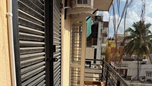 A narrow balcony with a checkered floor, a closed black shutter door, and a metal railing. - Soothing 3-bedroom apartment with AC in Bengaluru (Bengaluru)