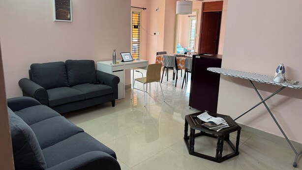 A living room with a sofa, a small table with papers, a desk with a laptop, and a dining area in the background. - Soothing 3-bedroom apartment with AC in Bengaluru (Bengaluru)