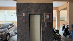 An elevator in a building with a granite wall, a parking area with cars and a bicycle, and a visible door number. - Soothing 3-bedroom apartment with AC in Bengaluru (Bengaluru)