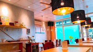 Ein modernes Café-Interieur mit Holztischen und -stühlen, Pendelleuchten und einem großen Fenster mit Blick hinaus.