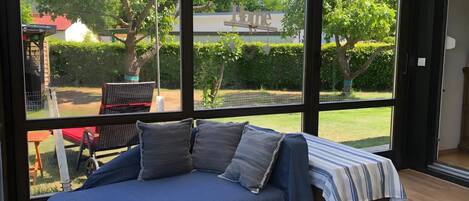 A room with a large window, a bed with a blue bedspread, and a view of a garden and trees.
