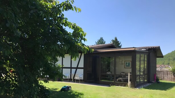Una casa con un amplio ventanal, un jardín y un árbol.