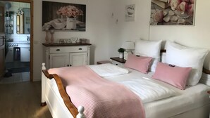Un dormitorio con cama, mesitas de noche, cómoda y un cuadro de flores.