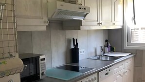 Una cocina con muebles blancos, microondas, estufa y pileta.