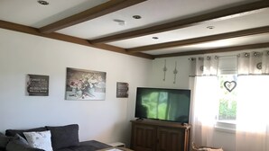 Una sala de estar con sofá, una mesa de centro, televisor y una ventana con cortinas.