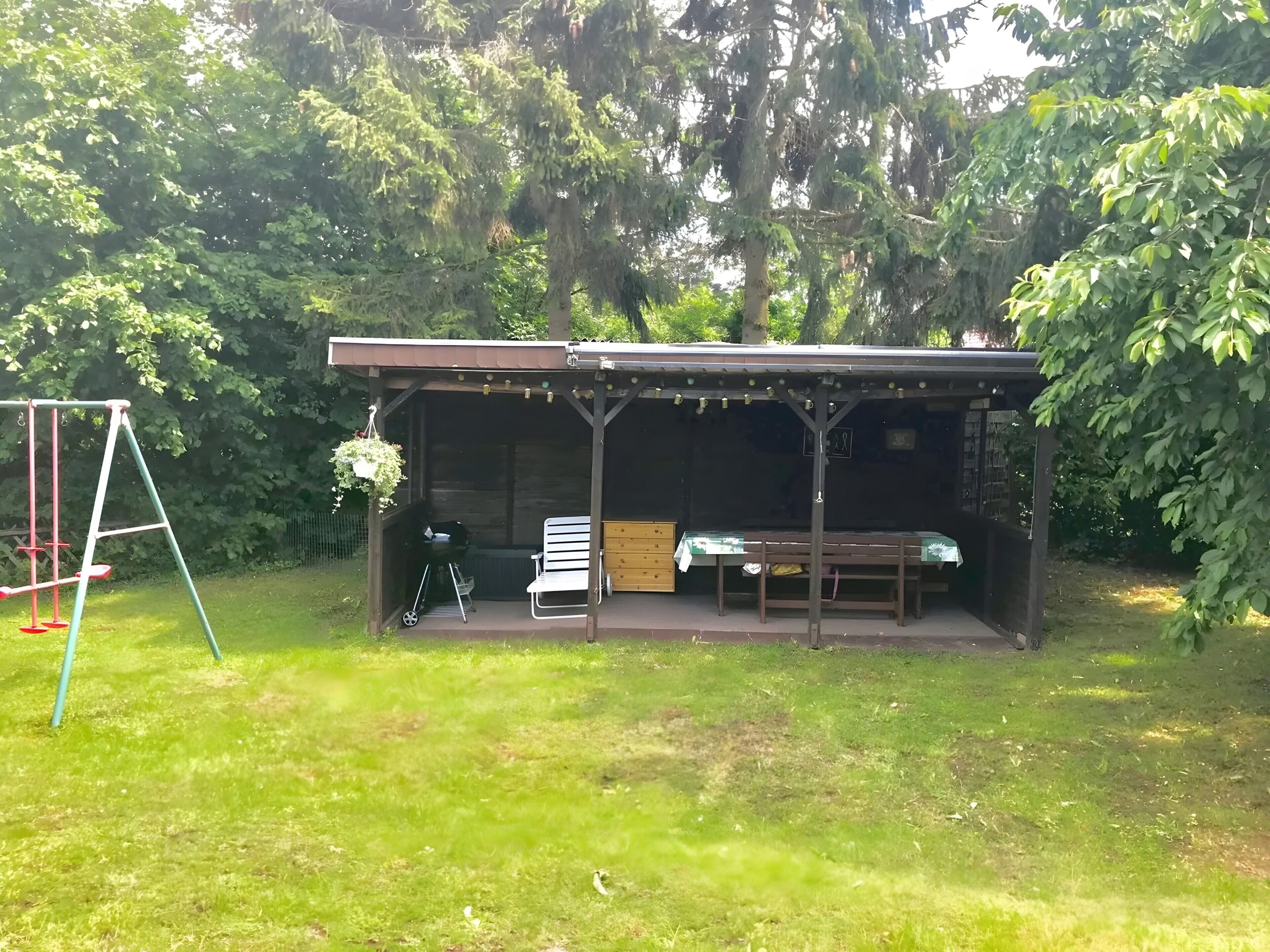 Un espace extérieur abrité, doté d’une table et de bancs, et entouré d’arbres.