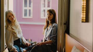 Two people sitting by a window with a view of a building.