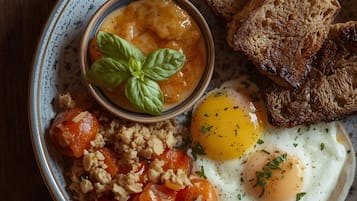 A plate with scrambled eggs, toast, and a small bowl of tomato sauce.