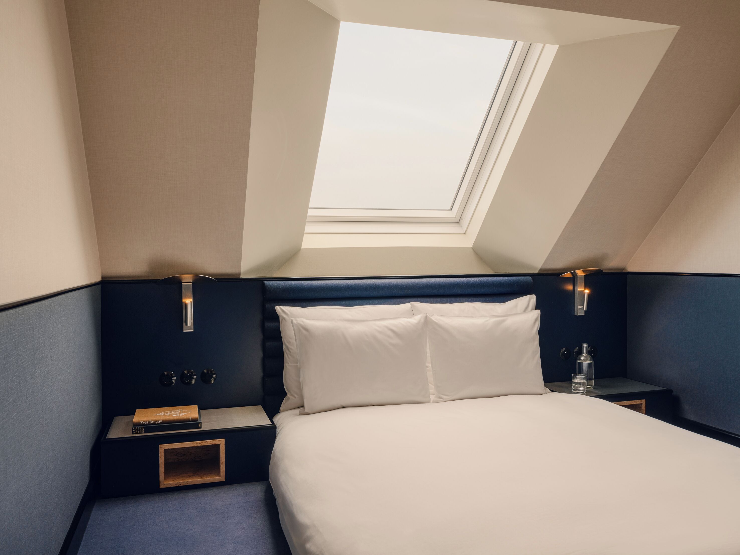 Ein Schlafzimmer mit Dachfenster, einem Bett, einem Nachttisch und einem Beistelltisch.