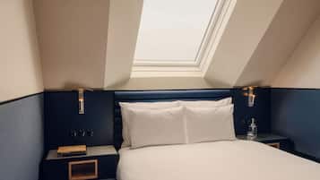 Un dormitorio con tragaluz, una cama, una mesita de noche y un buró.
