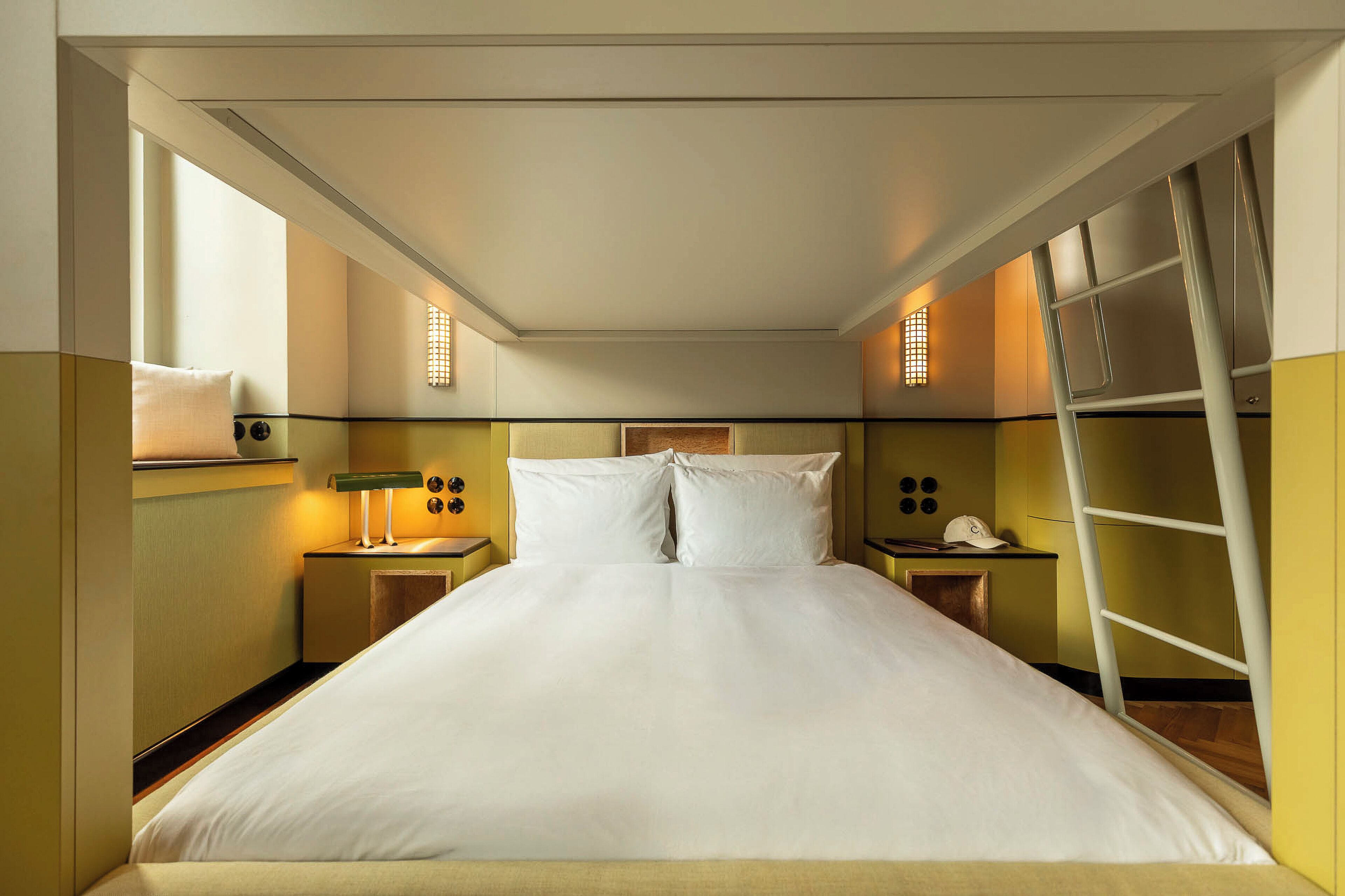 Habitación de hotel con cama, lámparas de noche, mesita de noche, teléfono en la pared y una escalera.
