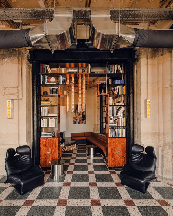 A library with bookshelves, a checkered floor, leather chairs, and a central seating area.